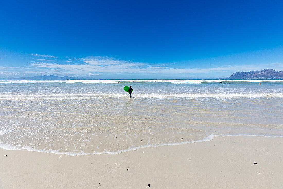 Boy (10-11) with surfboard running on empty beach