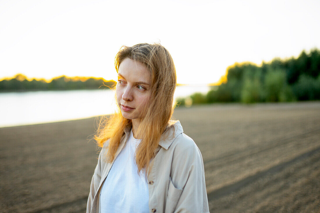 Porträt einer nachdenklichen Frau, die bei Sonnenuntergang am Strand steht