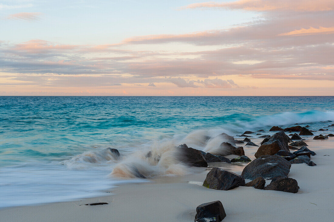 Die Brandung des Indischen Ozeans prallt bei Sonnenuntergang an einem tropischen Strand auf die Felsen. Anse Bambous Strand, Fregate Insel, Seychellen.