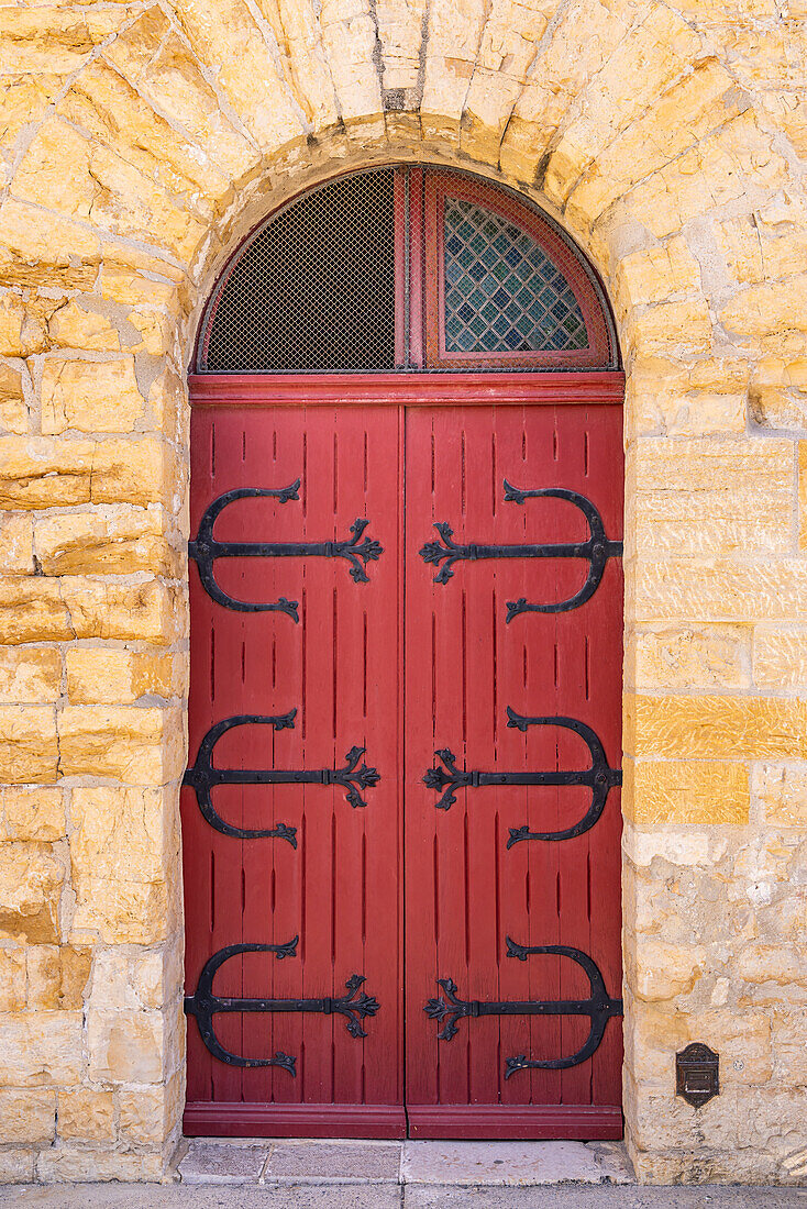 Saintes-Maries-de-la-Mer, Bouches-du-Rhone, Provence-Alpes-Cote d'Azur, Frankreich. Rote Tür mit Metallscharnieren in einem Steingebäude.