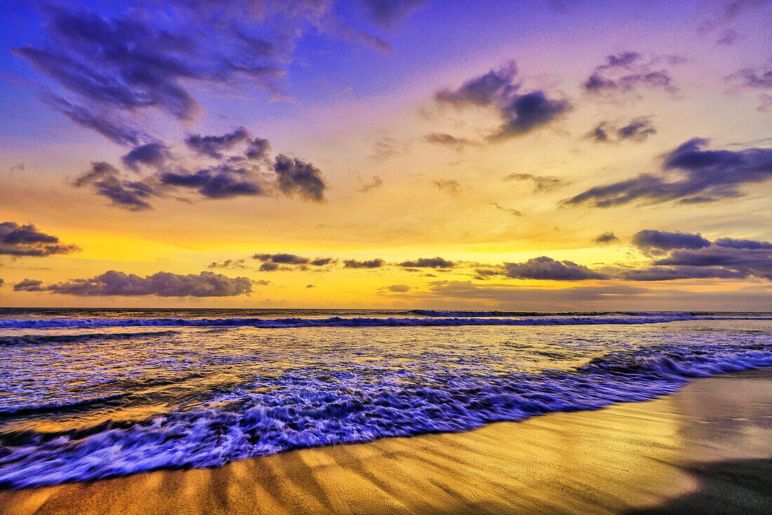 Das goldene Licht der untergehenden Sonne reflektiert einen goldenen Schimmer auf dem Strand von Pererenan Beach, während die Wellen auf Bali, Indonesien, anrollen