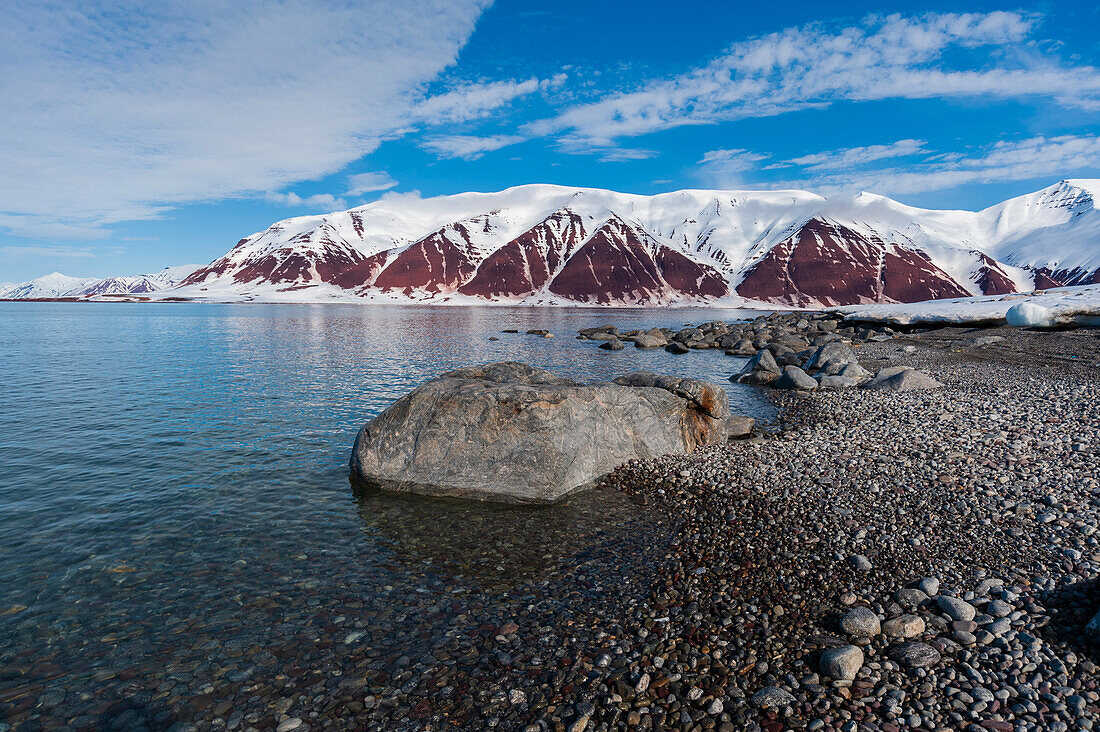 A gravel shoreline and snow covered mountains border Bockfjorden, Spitsbergen Island, Svalbard, Norway.