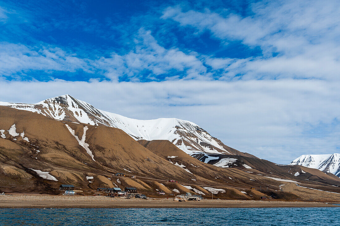 Snow streaked cliffs rise behind a small settlement near Longyearbyen on the bay of Adventfjorden. Spitsbergen Island, Svalbard, Norway.