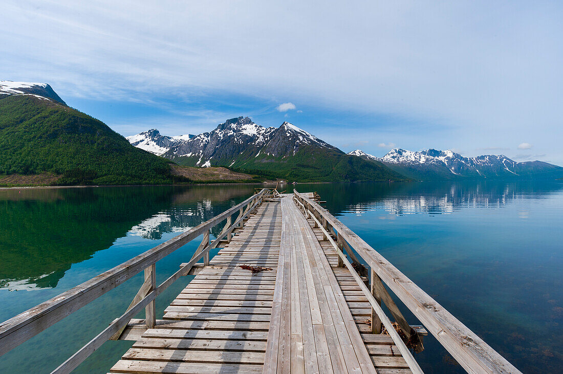 Ein Steg am Holandsfjord, der von eisbedeckten Bergen umgeben ist, in der Nähe von Svartisen. Saltfjellet-Svartisen-Nationalpark, Svartisen, Norwegen.