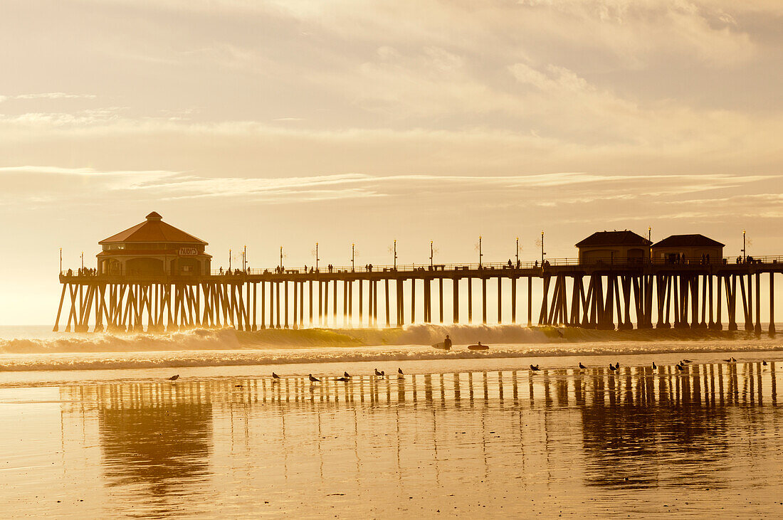 Der Pier von Huntington Beach und Surfer bei Sonnenuntergang. Huntington Beach, Kalifornien.