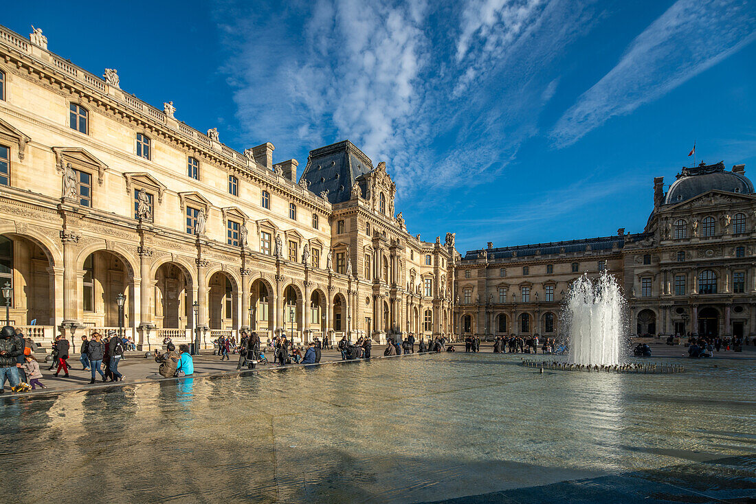 Besucher spazieren in der Nähe des Palais Royal unter einem klaren blauen Himmel.
