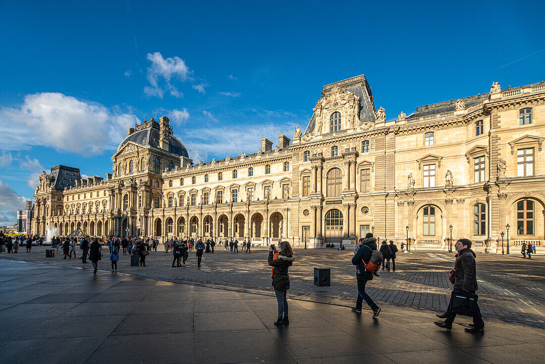 Besucher spazieren in der Nähe des Palais Royal unter einem klaren blauen Himmel.