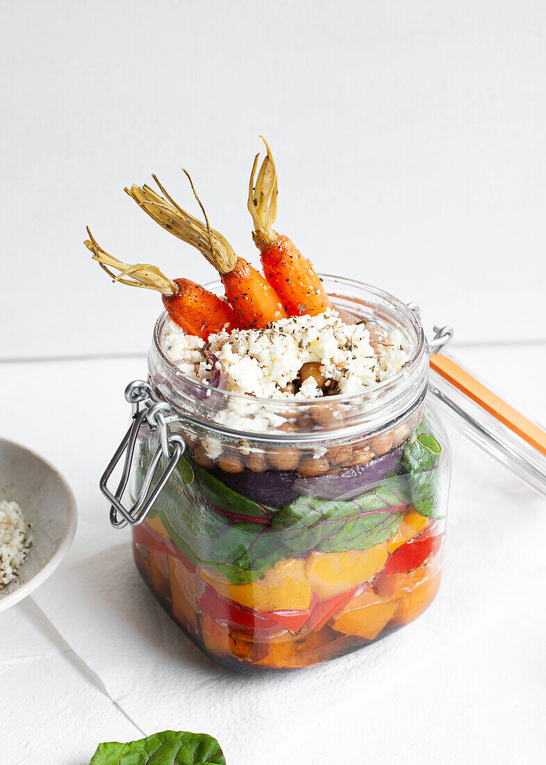 Salat mit bunten, reifen, gehackten Paprikaschoten und Bulgur mit rohen Karotten in einem Glas auf einem Tisch vor weißem Hintergrund