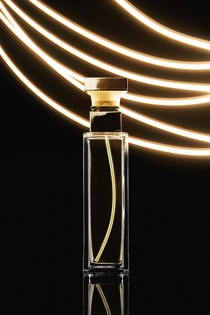Composition of stylish perfume bottle with golden lid placed on black background near luminous illumination