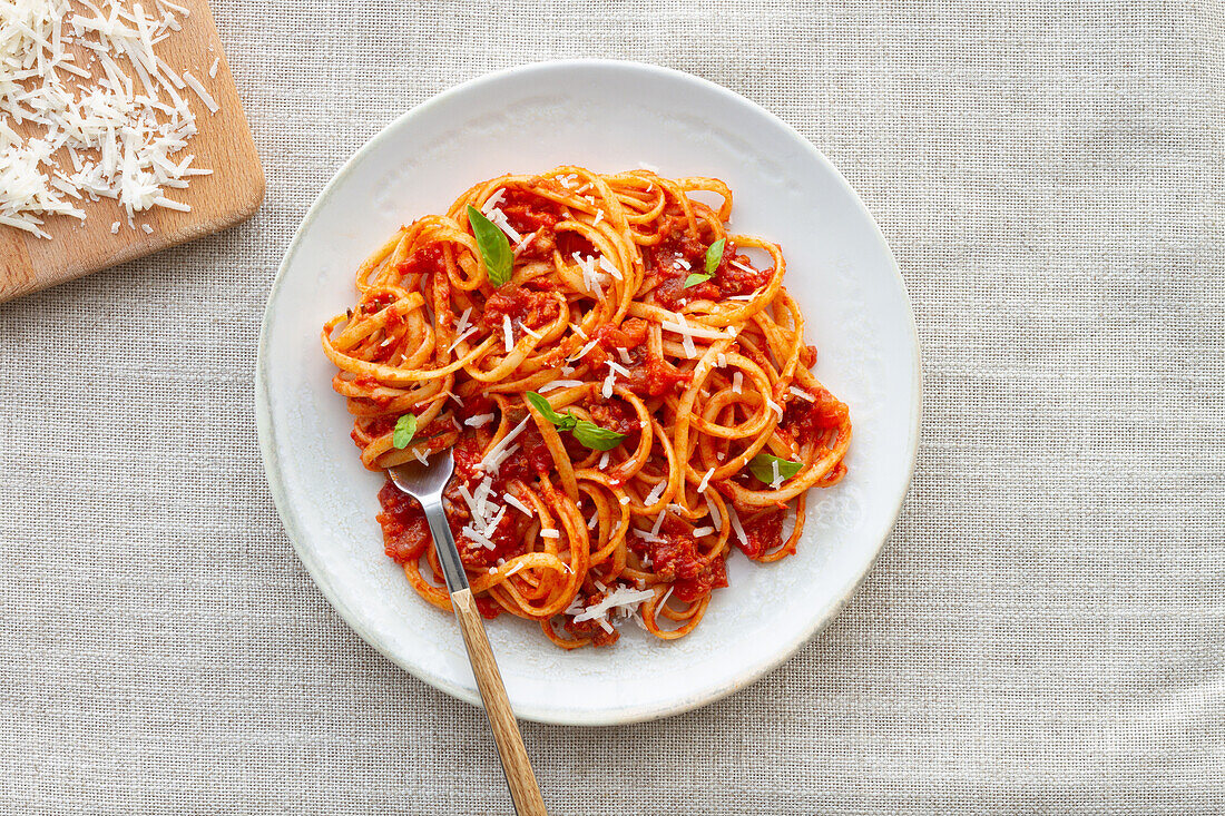 Blick von oben auf appetitliche hausgemachte Pasta mit Bolognesesoße, serviert mit frischen Basilikumblättern auf einem weißen Teller