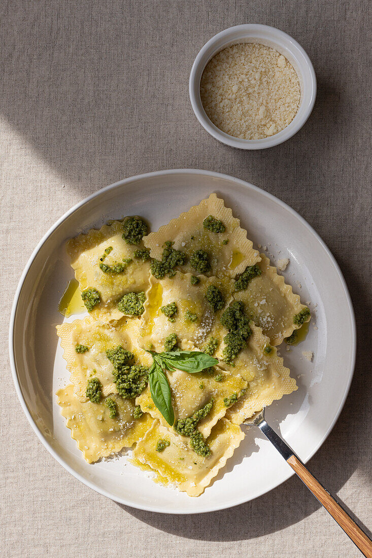 Draufsicht auf appetitliche gekochte Ravioli mit grüner Soße und Kräutern auf weißem Teller mit Gabel auf dem Tisch