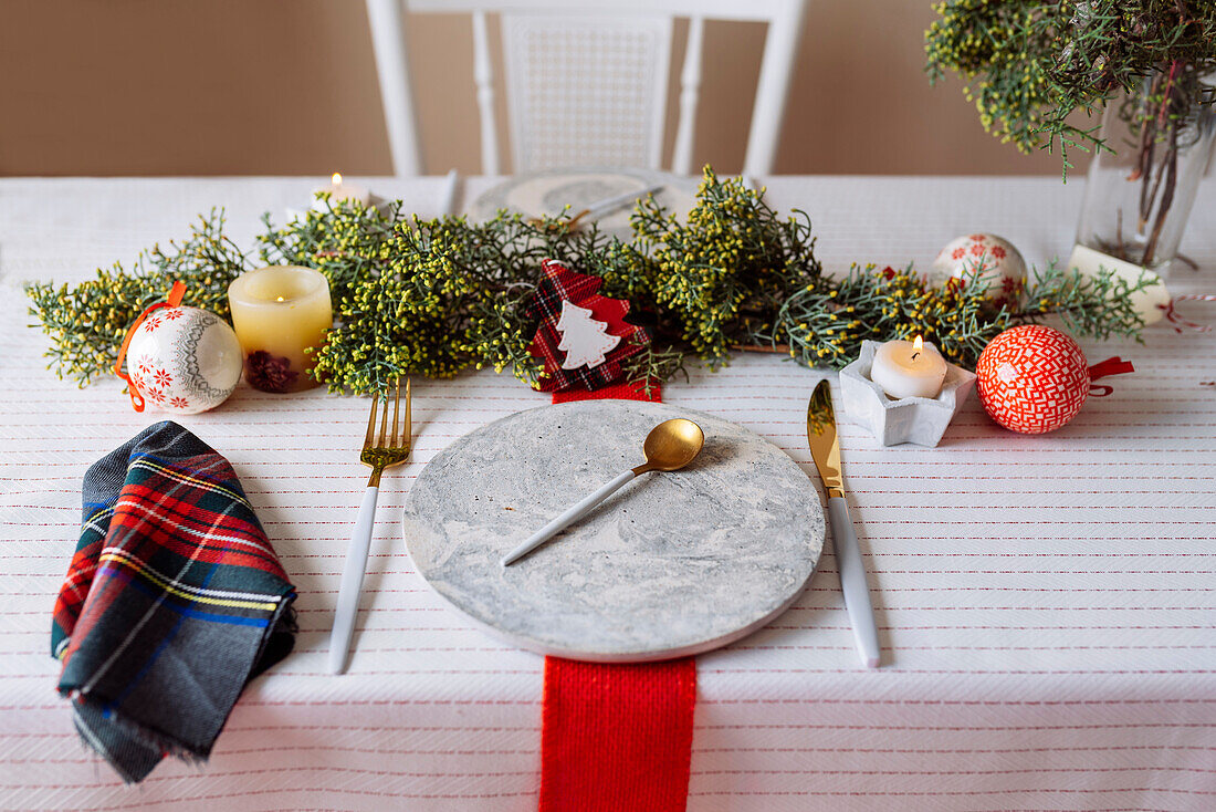 Von oben auf einen weihnachtlich gedeckten Tisch mit Kranzdekoration, rot und weiß, mit goldenem Besteck und Kerzen