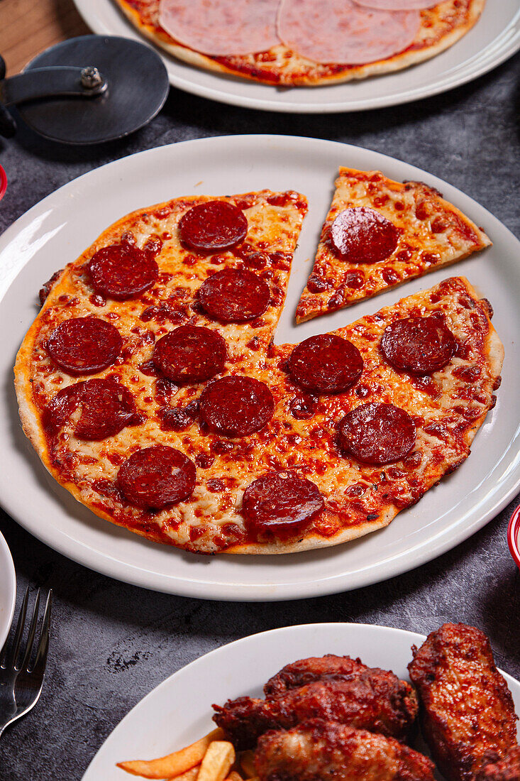 Blick von oben auf einen Teller mit leckerer Peperoni-Pizza und einer Schüssel mit Soße auf einem grauen Tisch beim Mittagessen