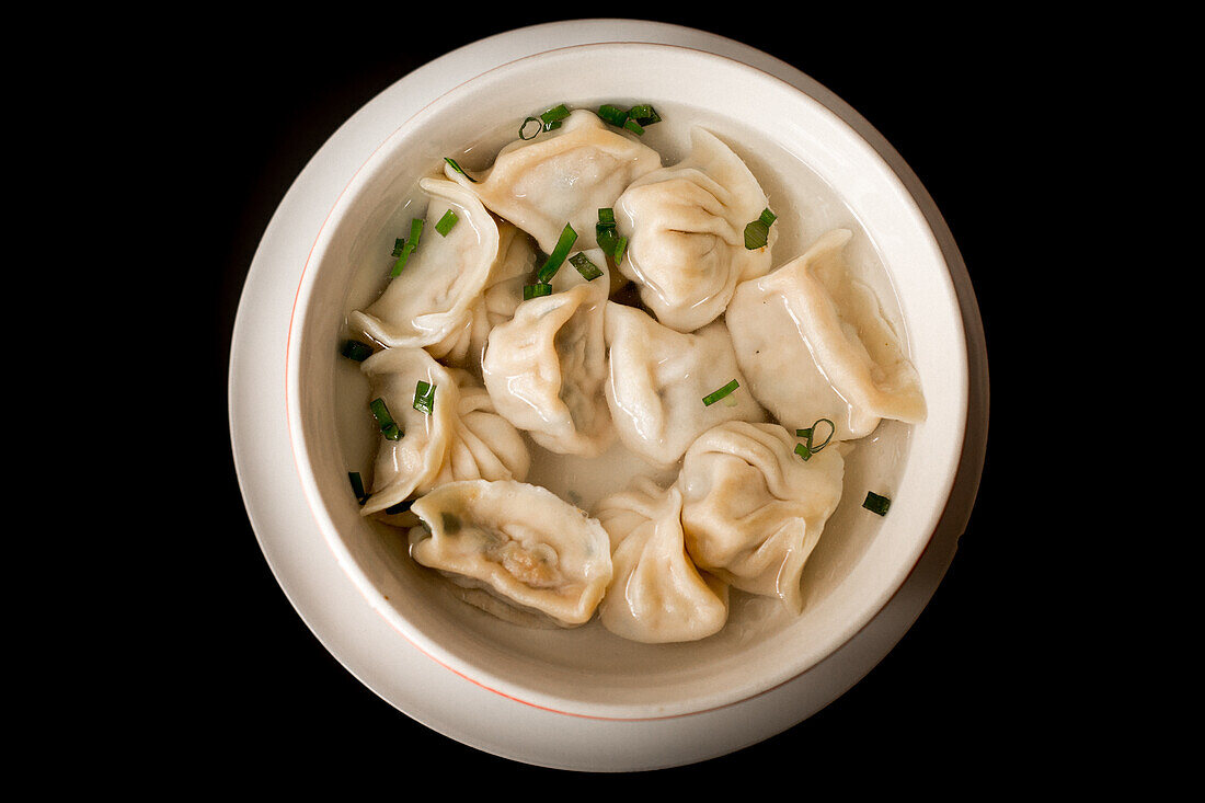 Nahaufnahme einer köstlichen Suppe mit Knödeln und Frühlingszwiebeln vor schwarzem Hintergrund