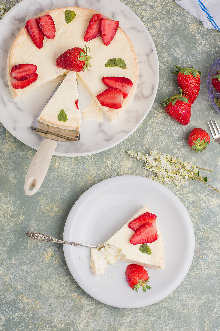 Slice of tasty sweet baked cheesecake with ripe strawberries served on white plate on table in light kitchen