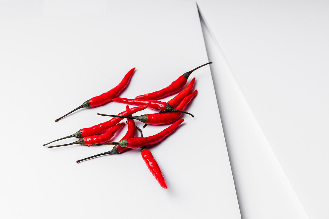 Scharfe rote Chilischoten auf einem Teller vor einem weißen, geometrischen Hintergrund