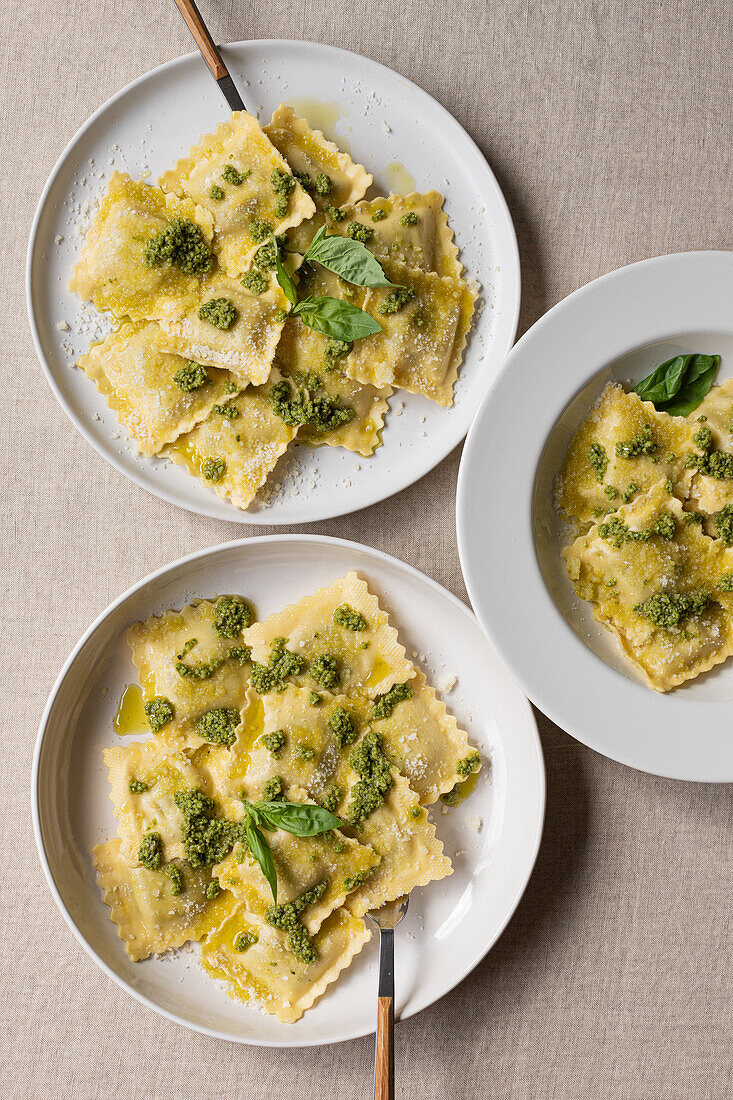 Draufsicht auf appetitlich gekochte Ravioli mit grüner Soße und Kräutern auf weißen Tellern mit Gabeln auf dem Tisch