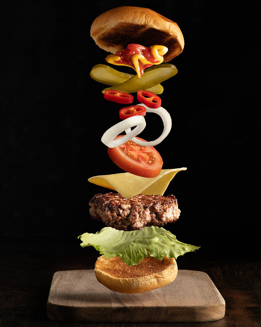 Fliegende Zutaten eines hochwertigen Fleisch-Burgers isoliert auf einem schlichten dunklen Hintergrund.