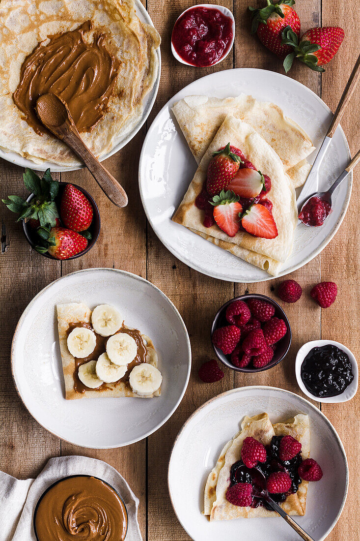 Von oben Teller mit leckeren Crêpes mit verschiedenen Belägen, die beim Frühstück auf einem Holztisch stehen