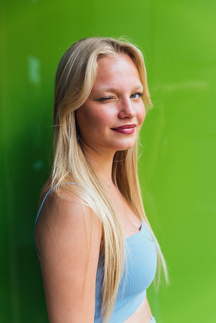 Seitenansicht einer koketten Frau mit blondem Haar, die der Kamera auf grünem Hintergrund zuzwinkert