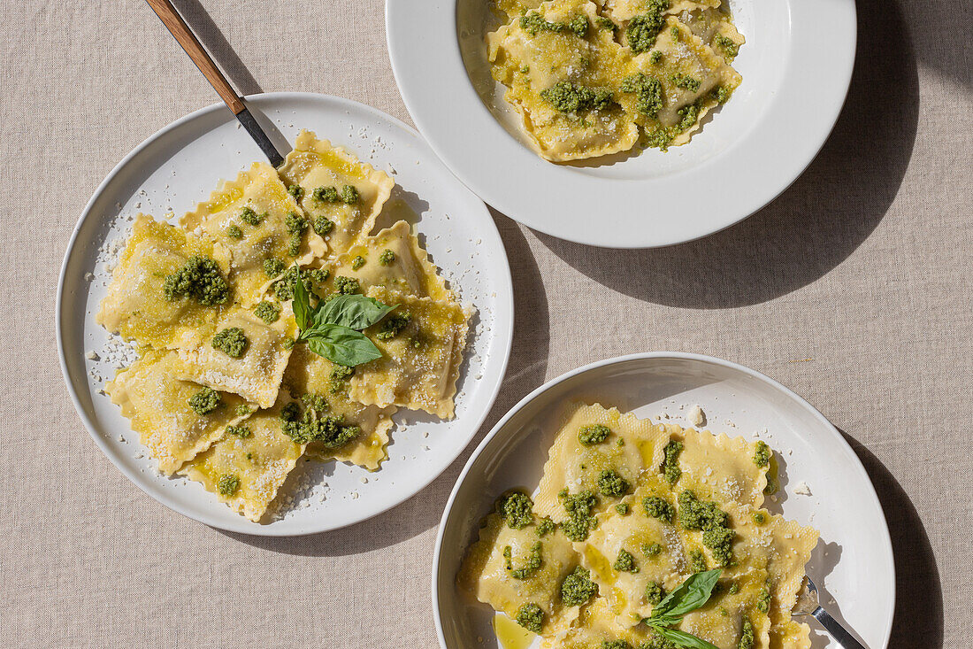 Draufsicht auf appetitlich gekochte Ravioli mit grüner Soße und Kräutern auf weißen Tellern mit Gabeln auf dem Tisch