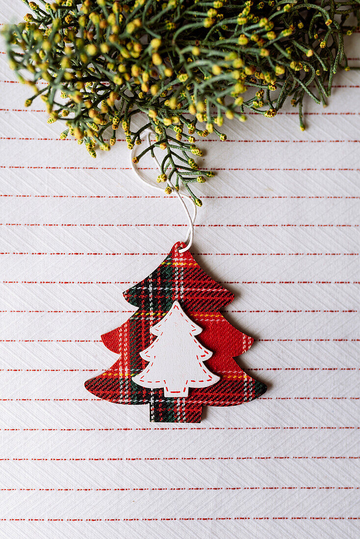 Pine tree hanging wooden ornament, red well plaid, decorated with branches on the tablecloth. Christmas concept