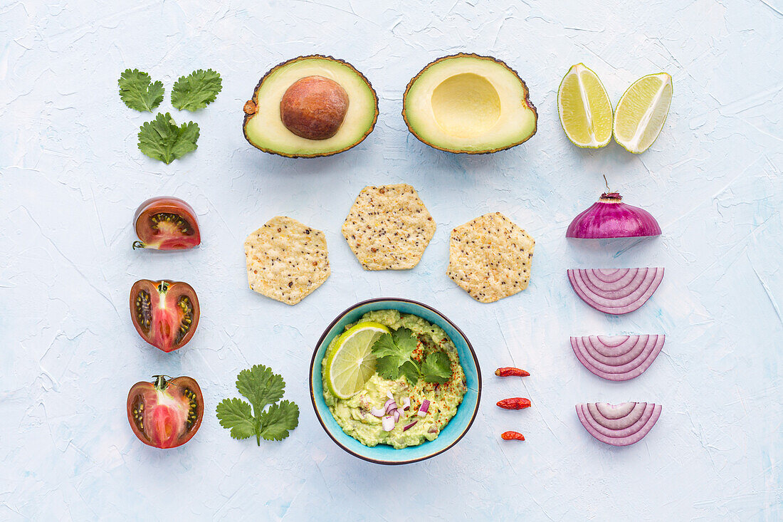 Flaches Bild von geschnittenen Tomaten und Zwiebeln mit Limette und Avocado auf weißer Fläche mit einer Schale frisch zubereiteter Guacamole