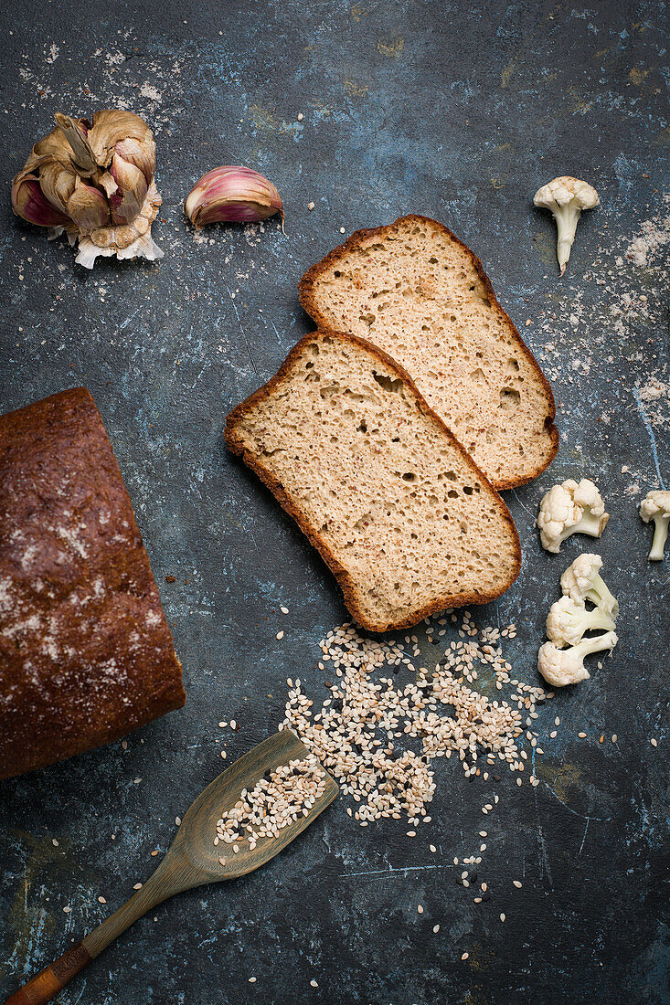 Draufsicht auf leckeres, frisch gebackenes Blumenkohlbrot auf einem Tisch mit Löffel in verstreutem Sesam in einer hellen Küche