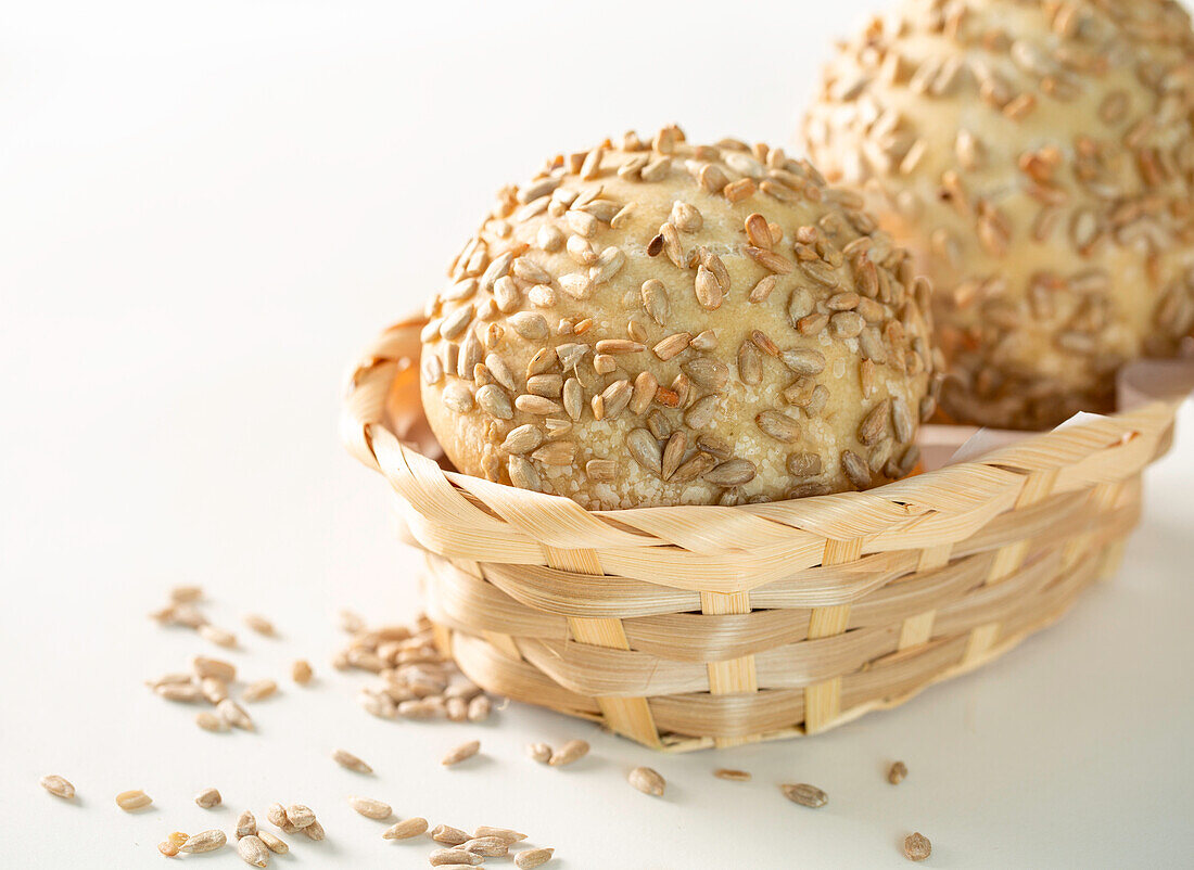 Hoher Winkel von frisch gebackenen Brötchen mit Sonnenblumenkernen, die in einer Korbschüssel auf weißem Hintergrund serviert werden