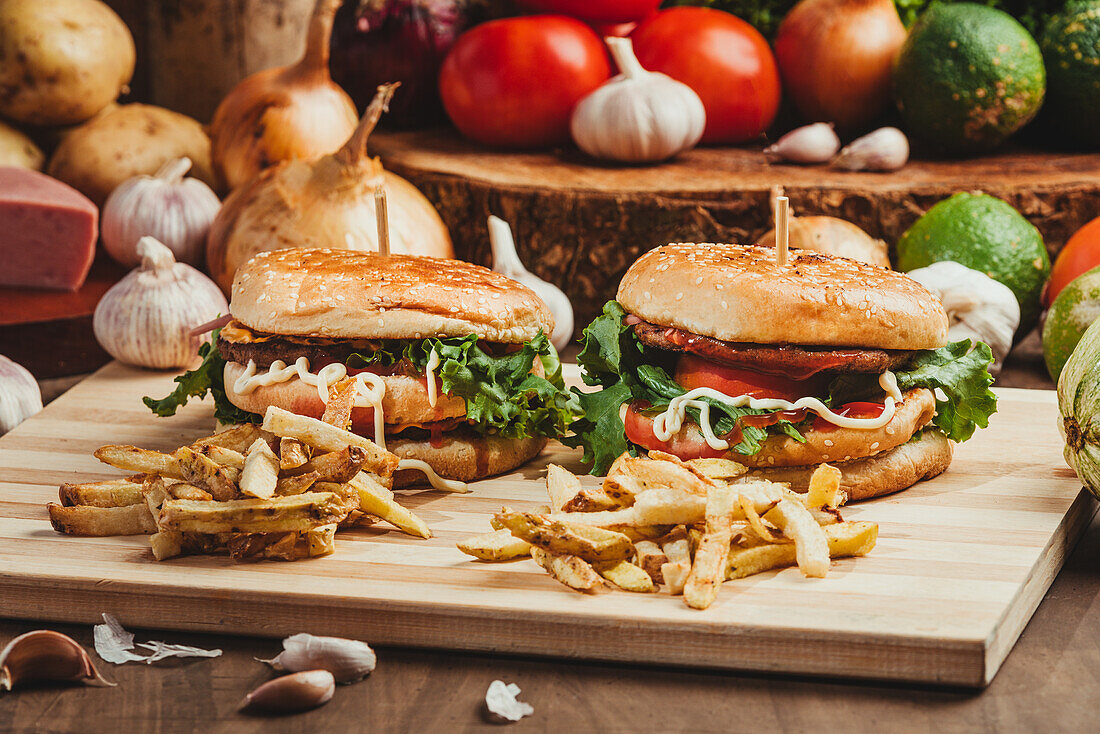 Appetitliche Hamburger mit Gemüse und Schnitzel auf einem Holzbrett mit Pommes frites in der Küche