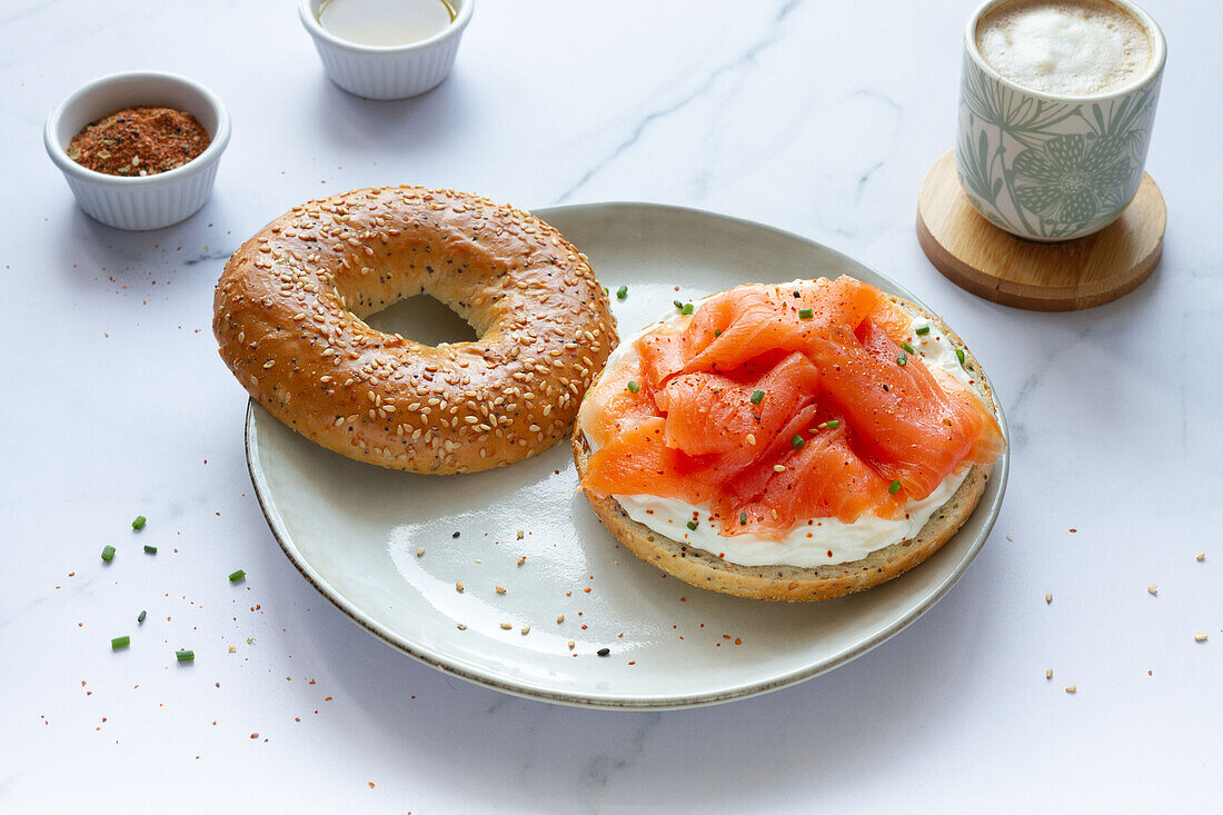 Frischer Bagel mit Käse und Lachs auf einem Teller, serviert auf einem Tisch mit einer Tasse heißem Kaffee in einer hellen Küche