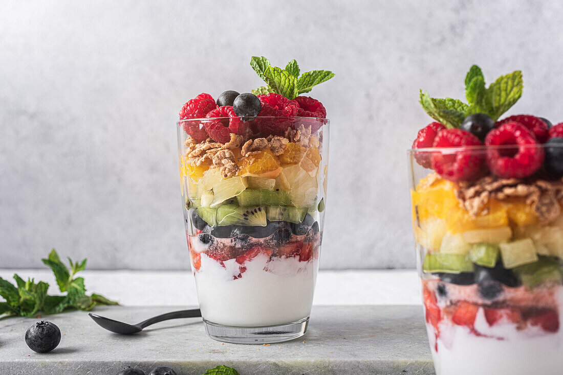 Appetitlicher Joghurt mit Schichten von frischen Früchten, serviert in Gläsern auf einem Tisch mit Minzblättern