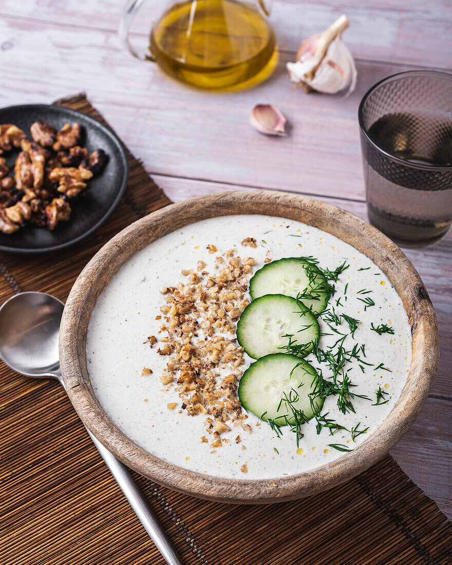 Schüssel mit traditioneller bulgarischer kalter Sommersuppe Tarator mit Joghurt neben einem Glas Wasser und einem Teller mit Nüssen von oben