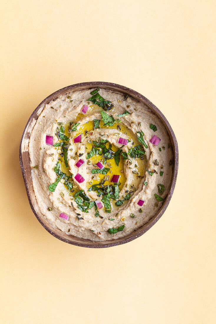 Appetitanregendes traditionelles Gericht Baba Ghanoush aus Auberginen und Kräutern in einer Schüssel auf beigem Hintergrund von oben