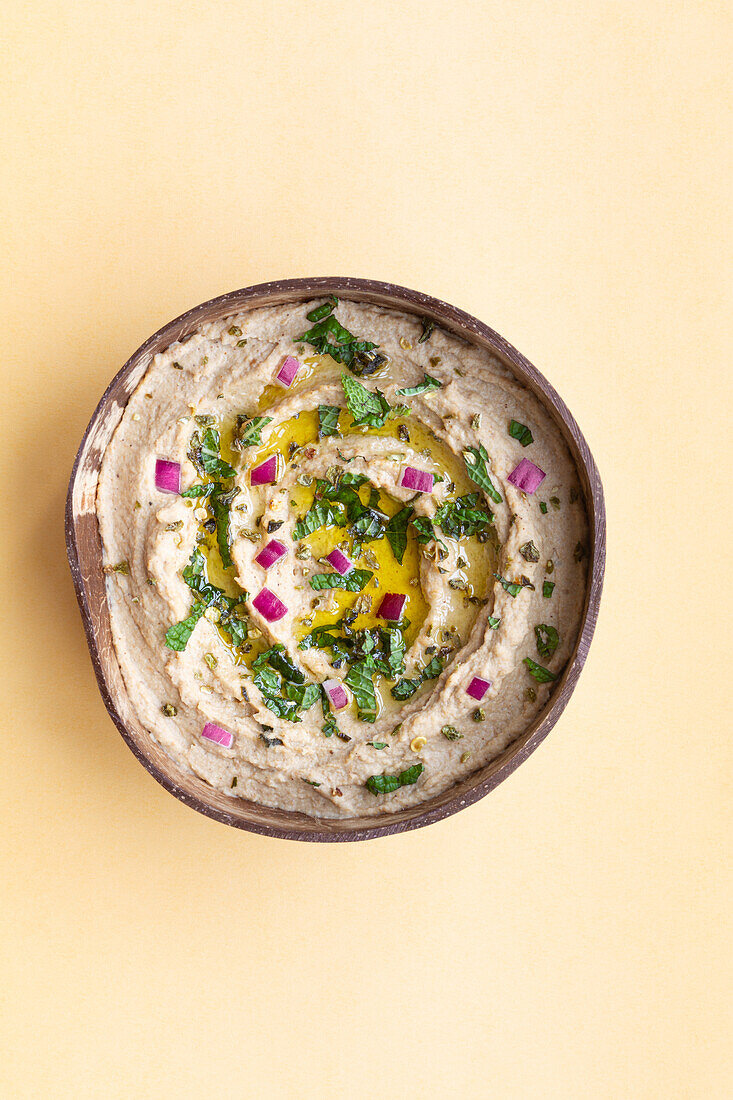 From above of appetizing traditional Baba ghanoush dish made of eggplants and garnished with herbs served in bowl on beige background