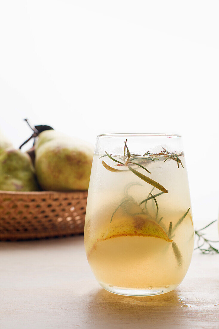 Cold pear cocktail in glass with rosemary and ice cubes placed on table with fresh fruits