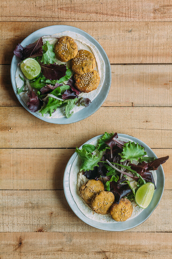 Teller mit frischem Salat und Süßkartoffel-Falafel neben Soße und Sesam auf Holztisch