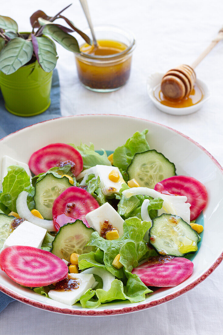 High angle of tasty vegetarian salad with cucumber and beetroot with green leaves and eggs with corn and sauce in bowl placed on table near dishware with honey