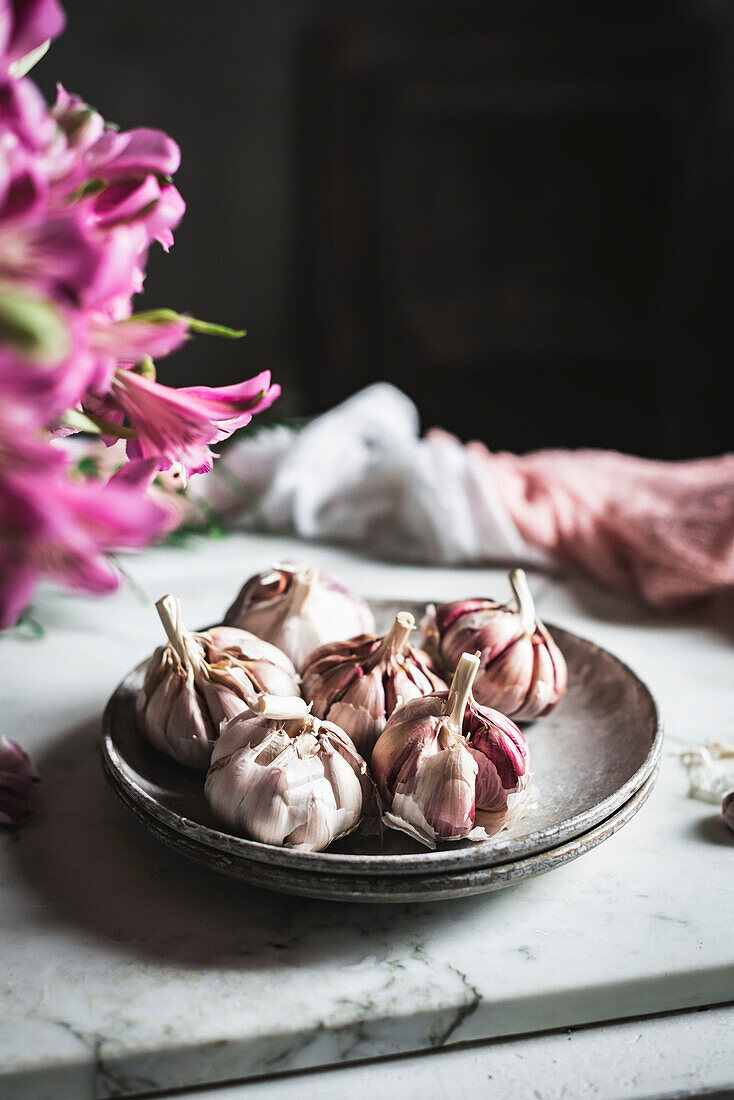 Cloves of unpeeled garlic on ceramic plate served with napkin on table in light kitchen