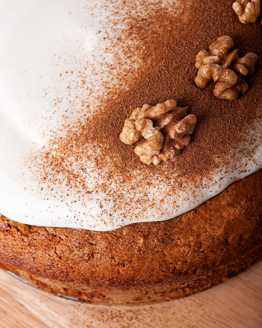 Close-up of tasty carrot cake with walnut and cinnamon powder on icing sugar glaze on light background