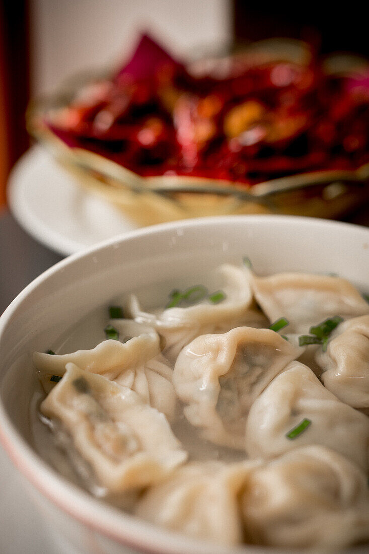 Nahaufnahme einer köstlichen Suppe mit Knödeln und Frühlingszwiebeln vor schwarzem Hintergrund