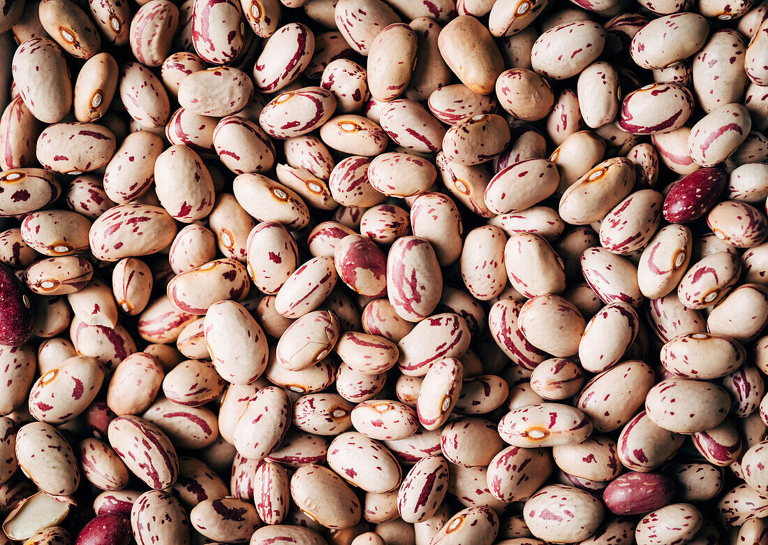 Top view full frame background of healthy dried uncooked white bean seeds with red spots stacked together in light kitchen