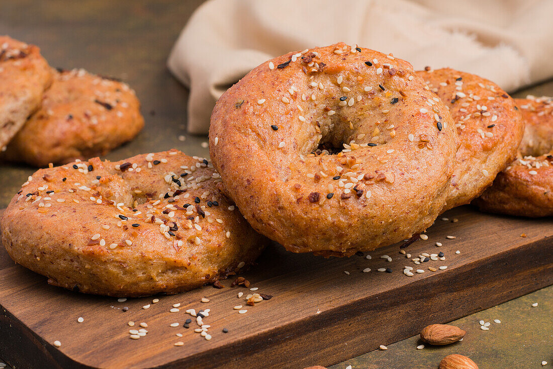 Leckere gebackene kohlenhydratarme Bagels auf einem hölzernen Schneidebrett auf einem Tisch mit Mandeln in einer hellen Küche