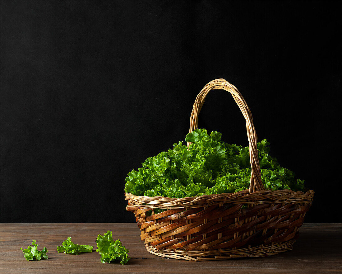 Weidenkorb mit grünen Blättern von frischem Salat auf dem Tisch auf schwarzem Hintergrund