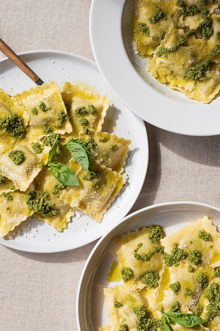 Von oben appetitlich gekochte Ravioli-Nudeln mit grüner Soße und Kräutern auf weißen Tellern mit Gabeln auf dem Tisch platziert