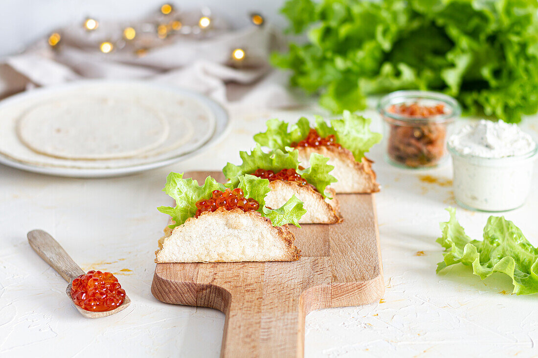 Kleine leckere Tacos mit rotem Kaviar und grünem Salat, serviert auf einem hölzernen Schneidebrett auf dem Tisch