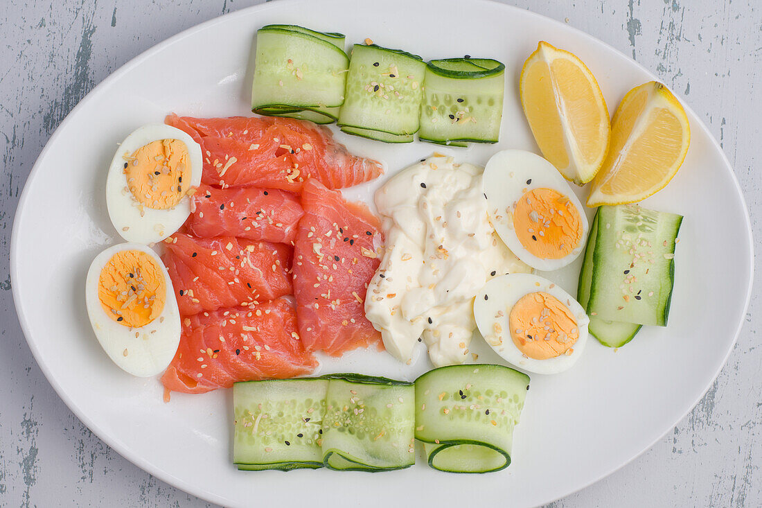 Geräucherter Lachs und Frischkäse auf einem Teller mit gekochten Eiern und Gurkenscheiben für ein schmackhaftes Mittagessen (von oben)