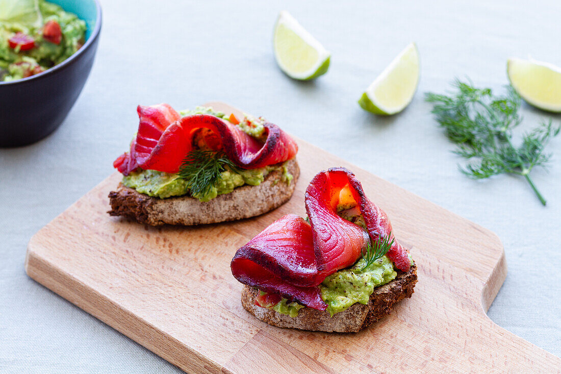 Tasty appetizers of rye bread toasts with avocado spread and smoked salmon slices with dill sprigs on chopping board