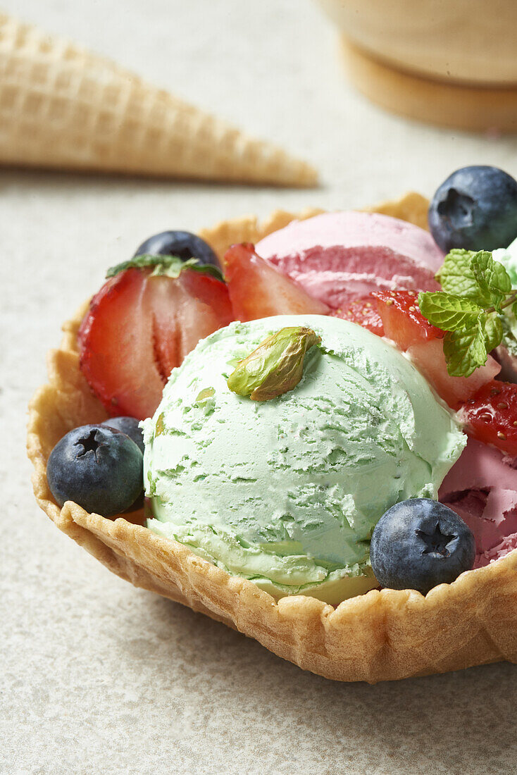 Blick von oben auf köstliches hausgemachtes Pistazien- und Erdbeereis in einer Waffelschale, dekoriert mit frischen Beeren, bei Tageslicht