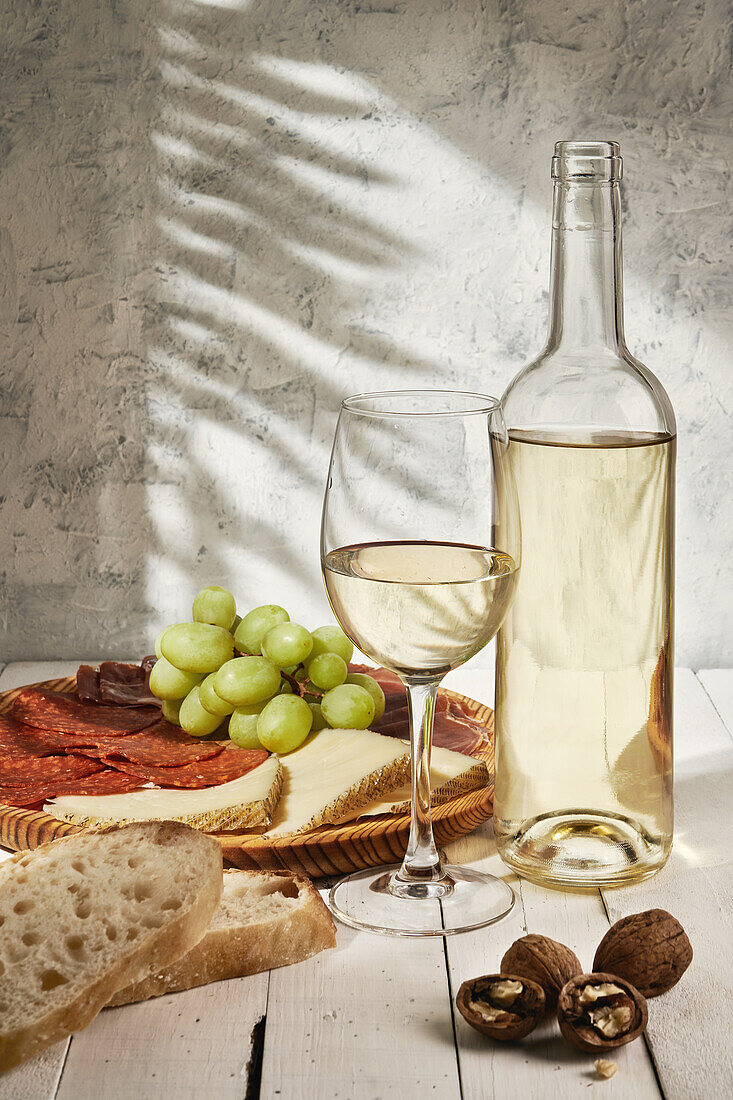 Komposition eines aromatisierten Weißweinglases, das auf einem Tisch neben einer Fleischplatte mit Weintrauben serviert wird